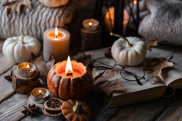 Fototapeta na wymiar Autumn composition with burning candles, mini munchkin pumpkins, warm wool knitted sweater on the wooden windowsill. Dark colours. Cozy home atmosphere, Thanksgiving decor, fall inspiration. Banner