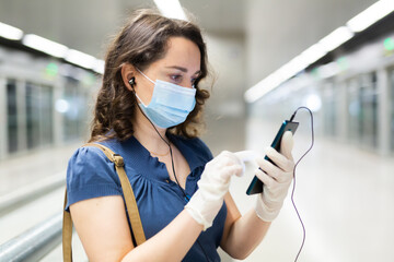 Attractive brunette in disposable medical mask and latex gloves using mobile phone while waiting...