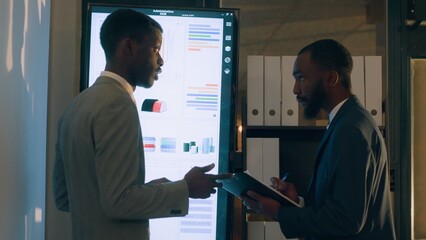 Manager looking at digital screen with employee, showing him researching key data needed for finding business insights and finishing project task. Company executives analyzing financial charts