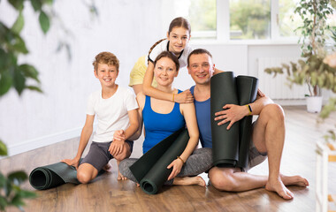 Happy family members sitting on the floor with black mats in hands in training room