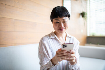 Young Asian woman using a smartphone on the couch at home