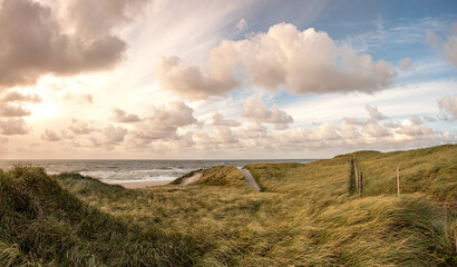Picturesque coastal landscape on the Danish North Sea coast with the sunset and beautiful sky with soft clouds and sun rays. In the dunes near Blavand with strong winds and waves on the beach. Holiday