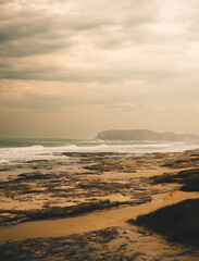Brazilian beach on evening. Cloudy sky with hills in the background and rocks in the sand. Rough seas. Torres - Brazil