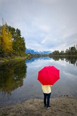 Holding a red umbrella by the river.