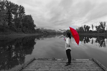 Black & White photo of woman on a dock with a red umbrella.