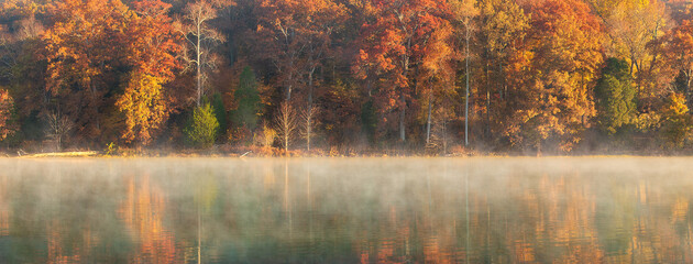 Autumn foliage in the morning from across a lake with light fog on the surface