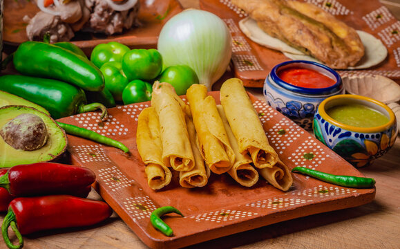 Comida mexicana, tacos dorados echos de tortilla rellenos de pollo y cerdo, platillo mexicano sobre un plato de barro rodeado de chiles, salsas picantes y condimentos. Comida tradicional.  