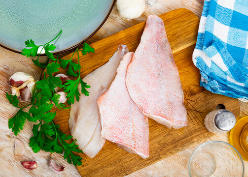 Fresh raw fillet of rockfish on wooden cutting board with aromatic herbs and garlic