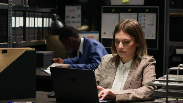 Focused female private detective using laptop to analyze confidential documents in criminal investigation. Caucasian investigator cross-checking crucial evidence and statements on personal computer.