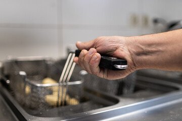 A hand holding the metal grill where croquettes are fried in boiling oil