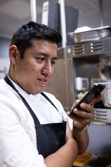 Vertical photo of a Latin chef looking at his mobile phone while he is at work