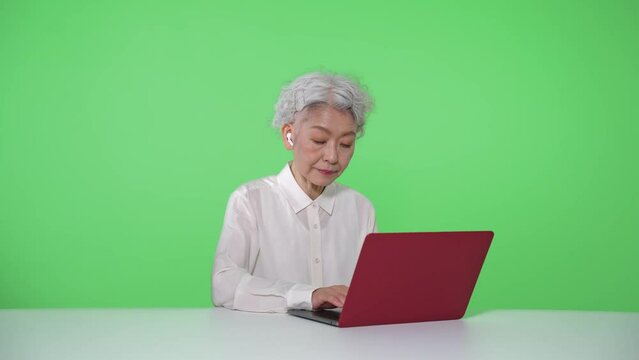 ノートパソコンを使うシニア女性　クロマキー合成用グリーンバック