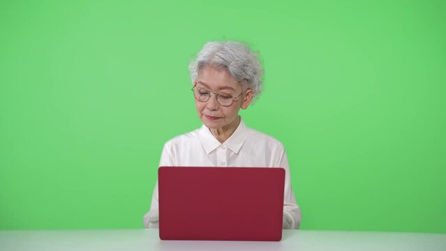 ノートパソコンを使うシニア女性　クロマキー合成用グリーンバック