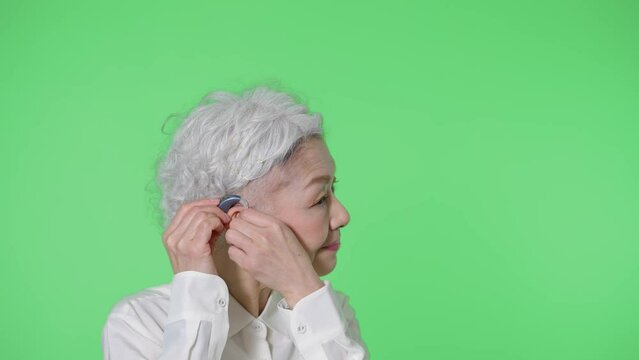 補聴器をつけるシニア女性　クロマキー合成用グリーンバック