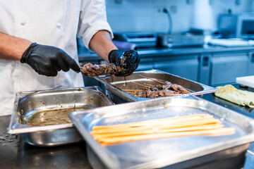 The hands of a chef with black gloves preparing veal skewers for the restaurant service