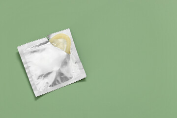 Condom in torn package on light green background, top view with space for text. Safe sex
