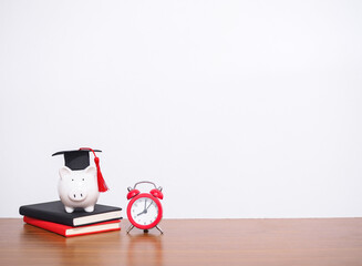 Piggy bank with graduation hat on hardcover book and red alarm. Copy space for text, Back to...