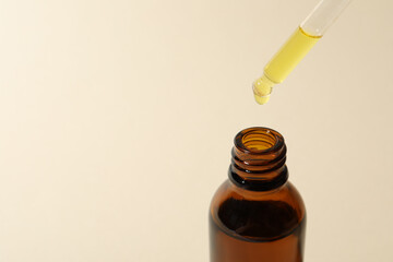 Dripping cosmetic oil from pipette into bottle on beige background, closeup. Space for text