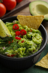 Delicious guacamole served with nachos chips on table, closeup