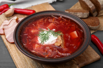 Tasty borscht with sour cream in bowl served on grey wooden table, closeup