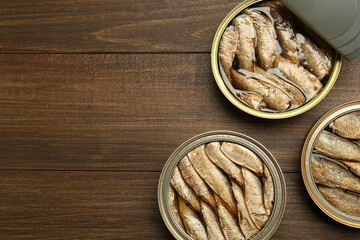 Fototapeta premium Open tin cans of sprats on wooden table, flat lay. Space for text