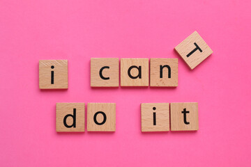 Motivation concept. Changing phrase from I Can't Do It into I Can Do It by removing wooden square with letter T on pink background, top view