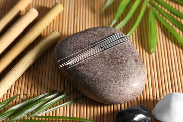 Stone with acupuncture needles on bamboo mat, above view - obrazy, fototapety, plakaty