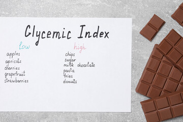 List with products of low and high glycemic index and chocolate on light grey table, top view