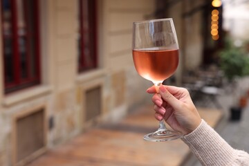 Woman holding glass of rose wine outdoors, closeup. Space for text