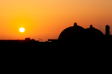 Silhouette of San Onofre nuclear power plant main reactors at sunset with sun visible.