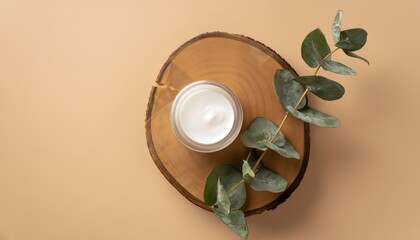 Top view of the transparent cream jar on a wooden stand and eucalyptus on an isolated beige background