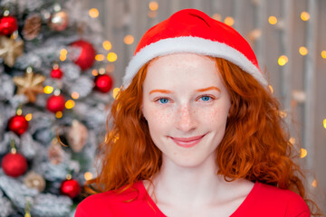 Christmas portrait of a beautiful young red-haired woman with blue eyes against the background of a Christmas tree