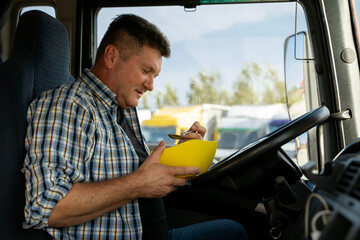 Trucker eating with spoon from bowl in truck cabin