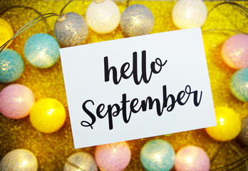 Hello September text on paper card with LED cotton balls decorate on yellow background