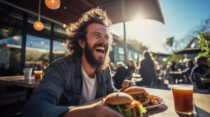 Rolgordijnen A happy man eating a burger in an outdoor restaurant as a Breakfast © sirisakboakaew
