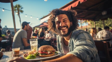 A happy man eating a burger in an outdoor restaurant as a Breakfast