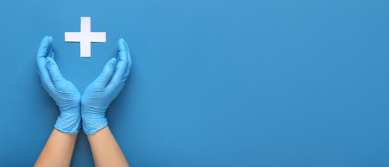 Doctor's hands with cross on blue background with space for text, top view.