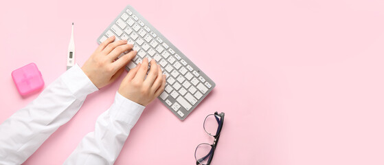 Doctor's hands with PC keyboard, pills and thermometer on pink background with space for text, top...