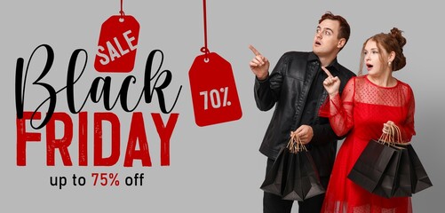 Surprised young couple with shopping bags pointing at text BLACK FRIDAY on grey background