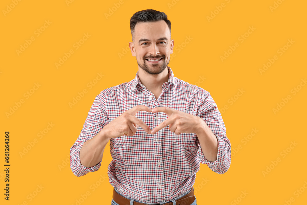 Poster Handsome man making heart with his hands on yellow background