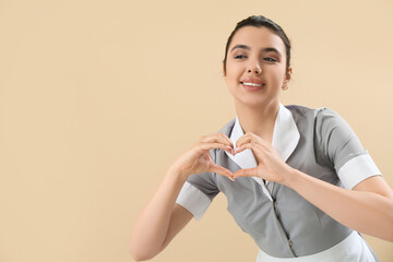Beautiful chambermaid making heart with her hands on beige background