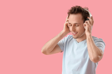 Fototapeta premium Young man in headphones listening to music on pink background