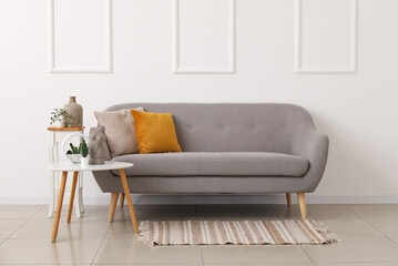 Cozy grey sofa with cushions and houseplants on tables near white wall