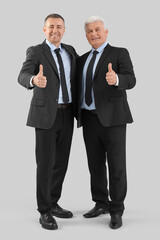Mature brothers in suits showing thumbs-up on grey background