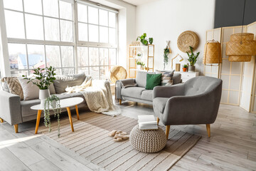 Interior of bright living room with cozy sofas and armchair near big window