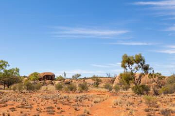 Granite boulders surrounded by drought resistant trees, bushes and grasses in a semi arid environment with blue sky background in Queensland, Australia.