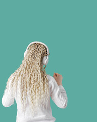 Modern stylish girl woman in headphones on head, listening to music and dancing, blonde long curly hair, back view, trend mint color background with copy space, minimal lifestyle no face