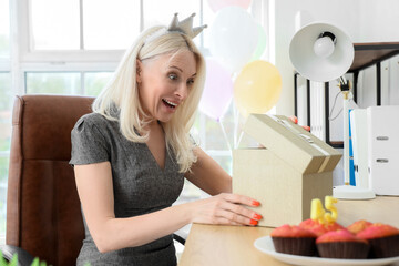 Mature woman opening birthday gift in office