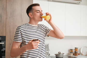 Fototapeta premium Young man with doughnut drinking orange juice in kitchen