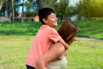 Young latina woman in the park playing with her young son on a sunny day.